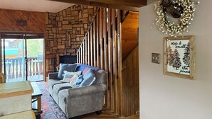 A cozy living room with a stone wall, a gray sofa, a wooden staircase, and a deer head decoration.