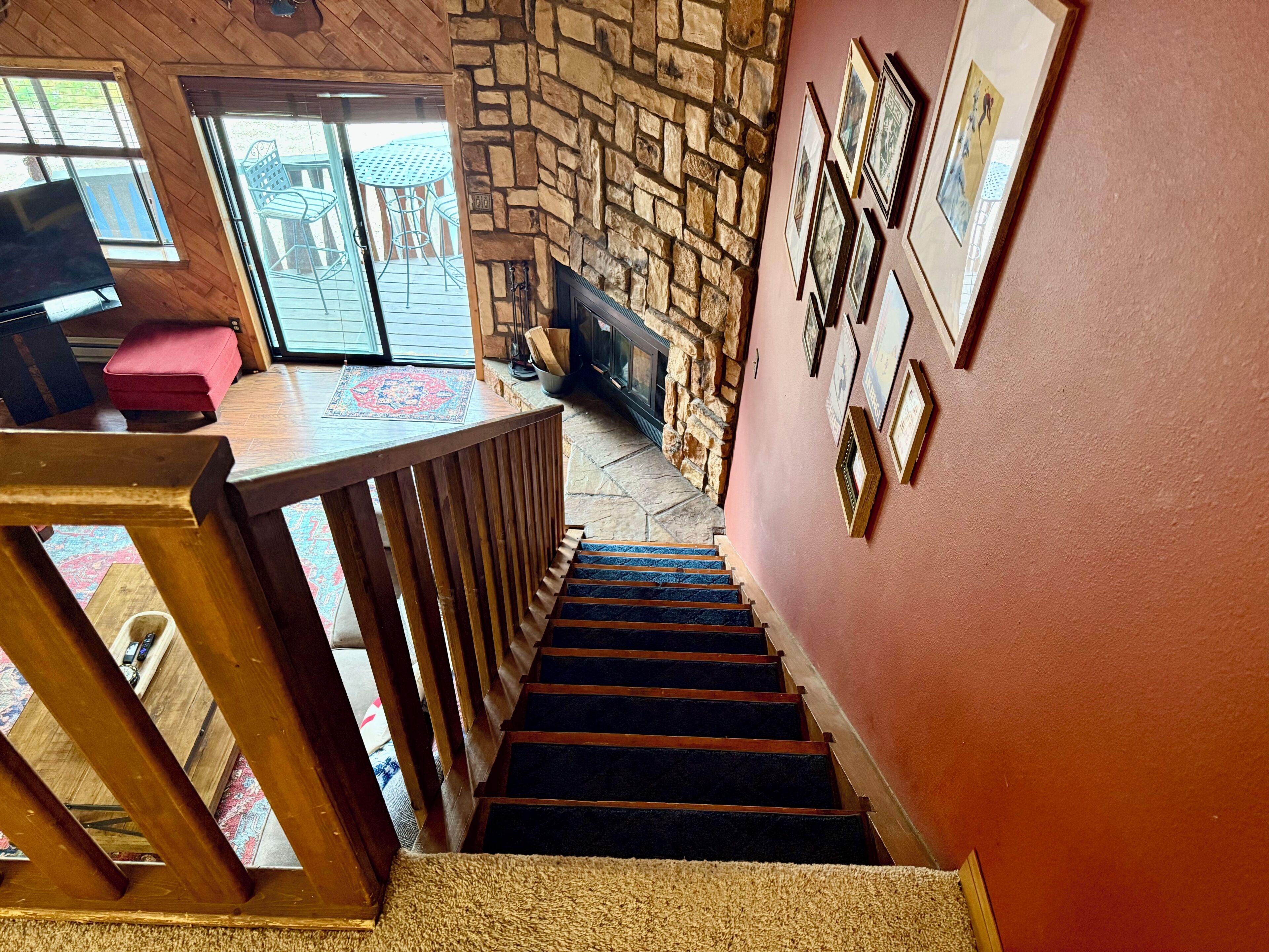 A staircase with a stone wall, wooden railing, and a red wall with framed pictures.