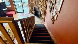 A staircase with a stone wall, wooden railing, and a red wall with framed pictures.