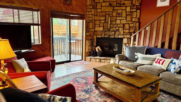 A cozy living room with a stone fireplace, a red sofa, a grey sofa with a 'SKI' pillow, and a wooden coffee table.