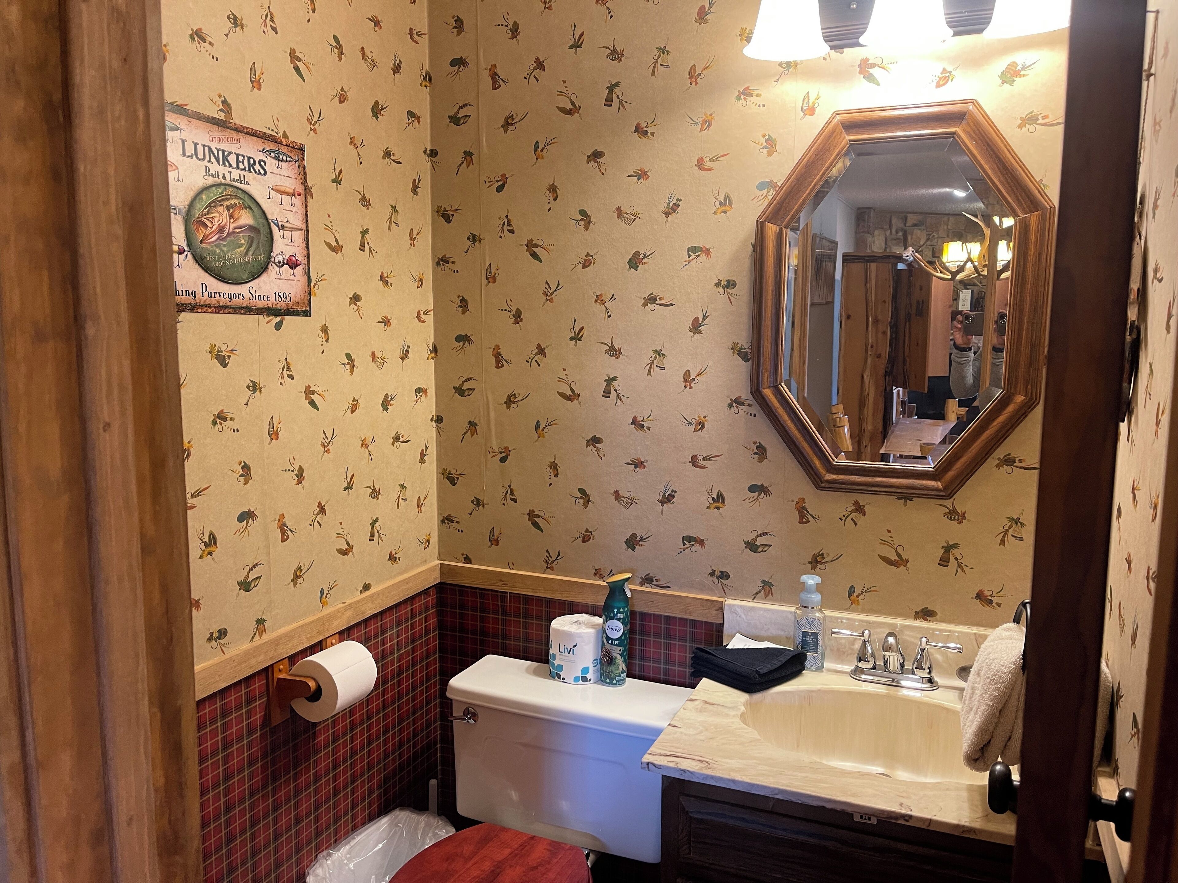 A bathroom with a toilet, sink, mirror, and patterned wallpaper.