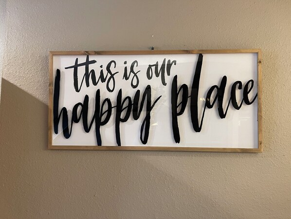 Un cartel en marco con el texto 'this is our happy place' sobre una pared color beige.