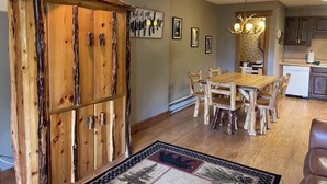 Een eethoek met een houten tafel en stoelen, een keuken op de achtergrond, en een decoratief vloerkleed.
