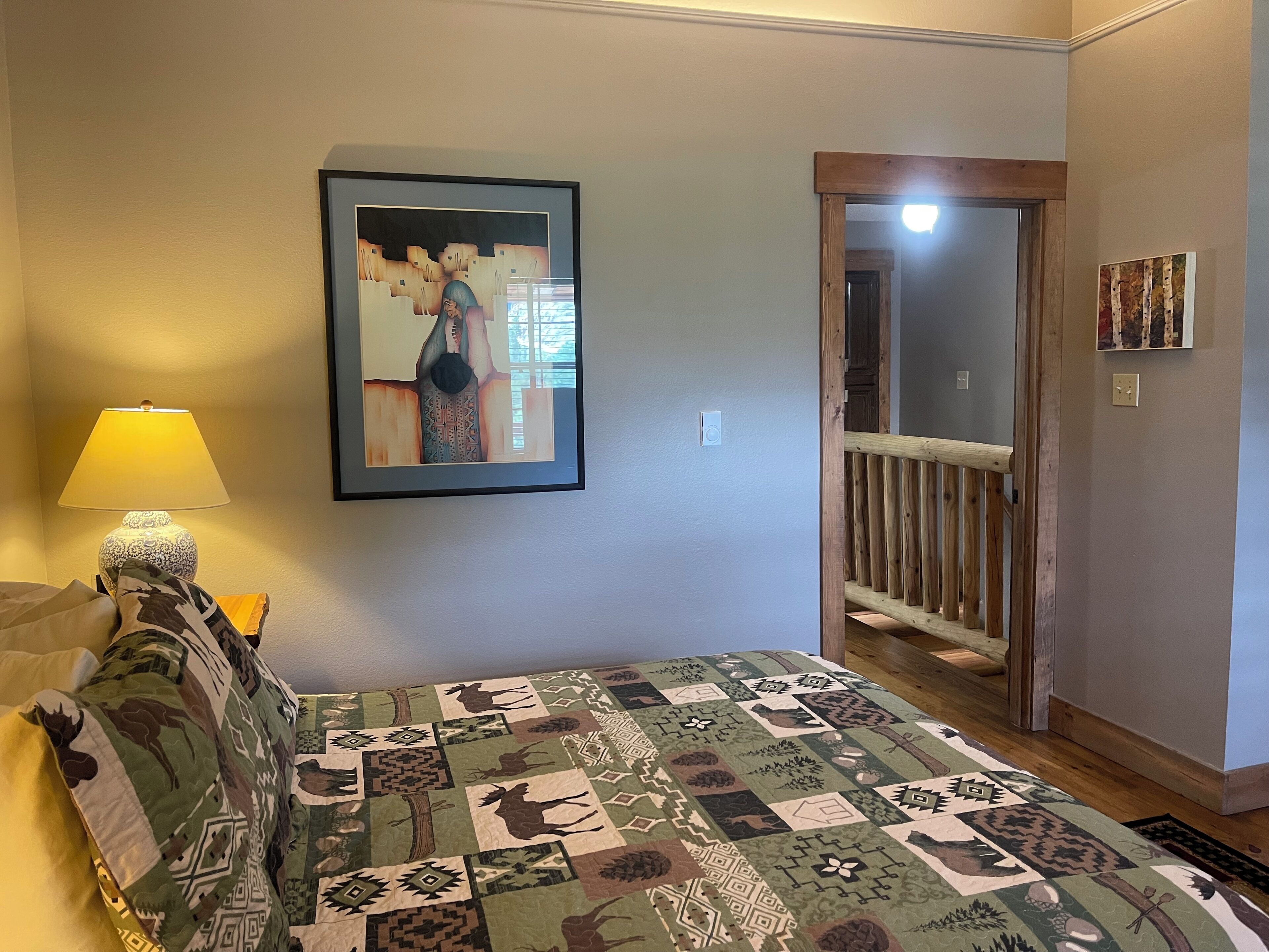A bedroom with a bed, a framed picture on the wall, a lamp, and a door leading to another room.