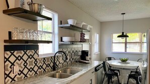 Una cocina con lavamanos, encimera y comedor con mesa y sillas.