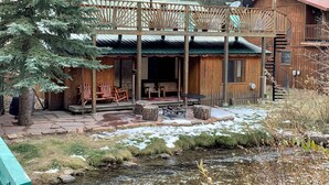 En stuga byggd av trä med en veranda, utomhusmöbler och utsikt över en bäck.