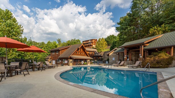 A pool area with lounge chairs and umbrellas, surrounded by wooden buildings and trees.