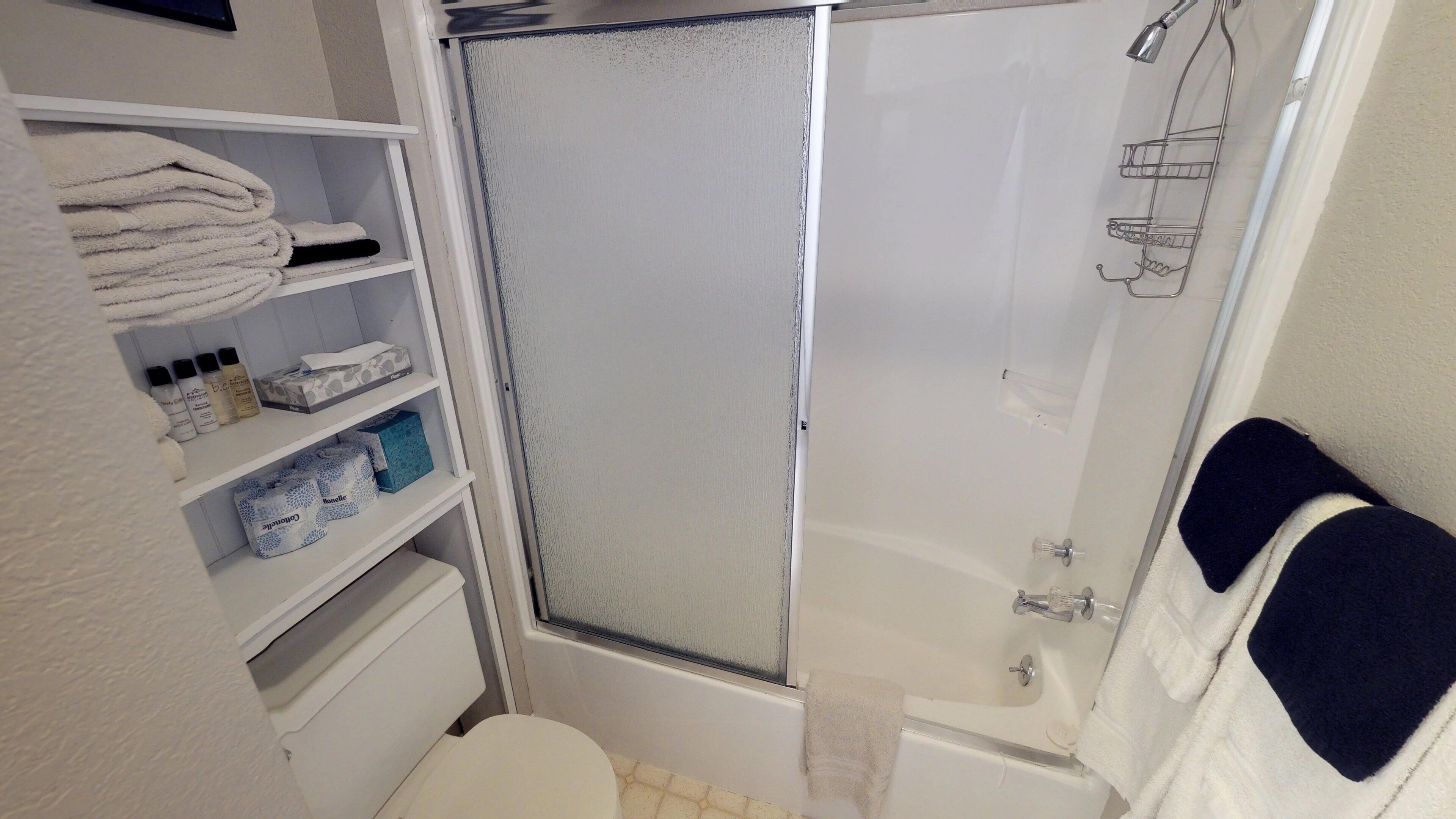 A bathroom with a shower, toilet, and shelves with toiletries.