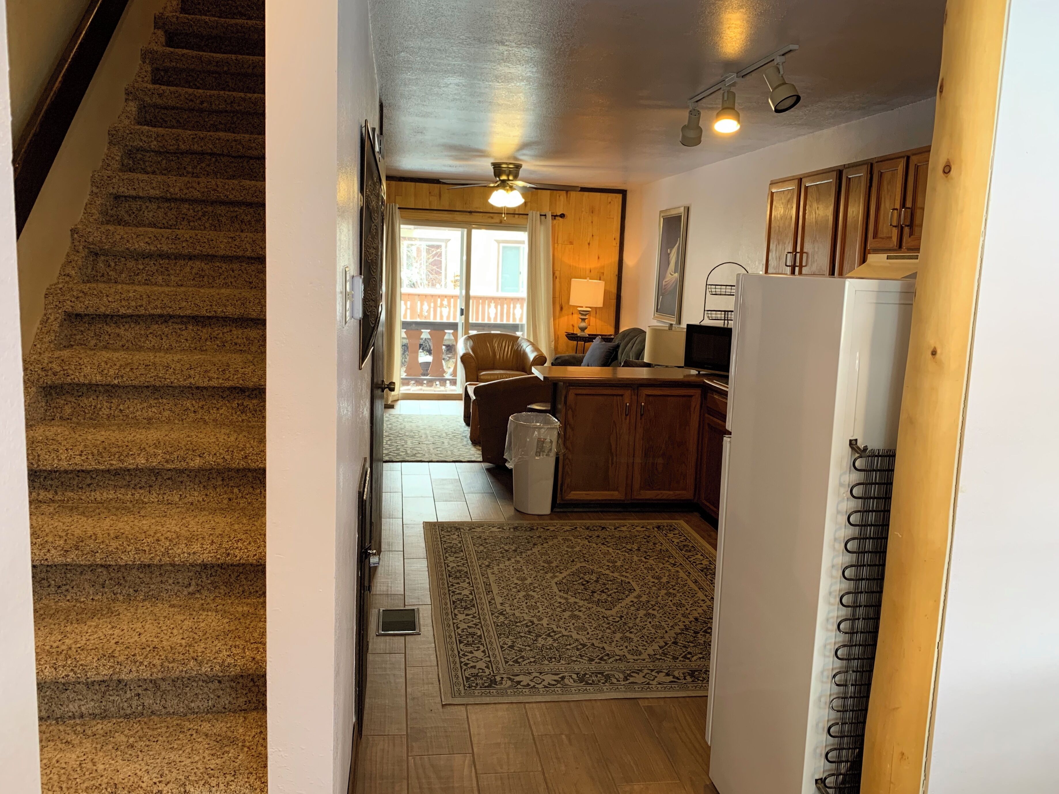 A staircase leading to a living area with a wooden floor, a rug, a sofa, a coffee table, and a refrigerator.