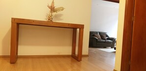 A wooden console table with a decorative item on top, a dark-colored sofa in the background, and a wooden floor.