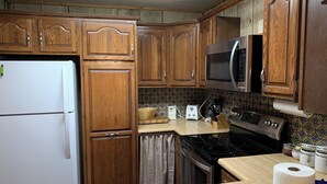A compact kitchen with wooden cabinets, a stainless steel microwave, a stove, and a refrigerator. - Casa Rio on the River (Red River)