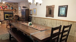 A dining area with a long wooden table, benches, and chairs. There is a fireplace with a mantel, shelves with decorations, and framed pictures on the wall. - Casa Rio on the River (Red River)