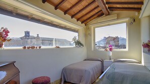 A bedroom with two beds, a wooden dresser, a small stool, and a window with a view of buildings. - Rinidia Siena Centro (Siena)