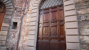 A large wooden double door with a metal grille above it, set in a building with a brick facade and a stone base. - Rinidia Siena Centro (Siena)