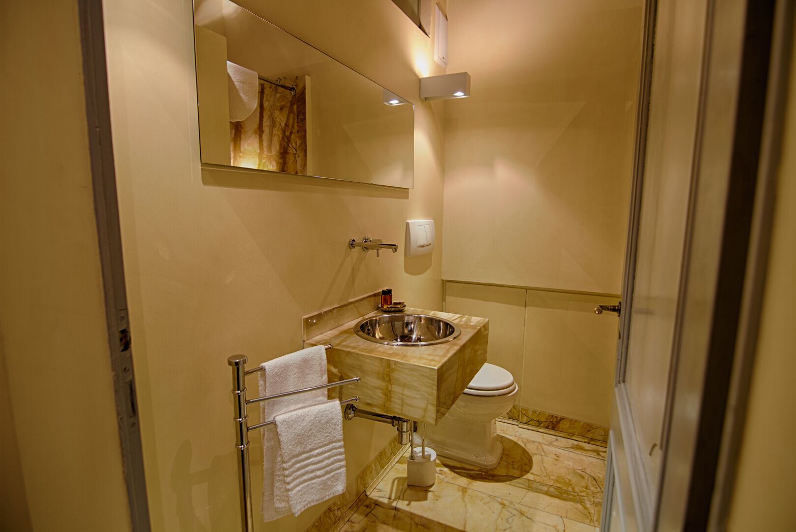 A bathroom with a marble sink, a toilet, a towel rack, and a mirror.
