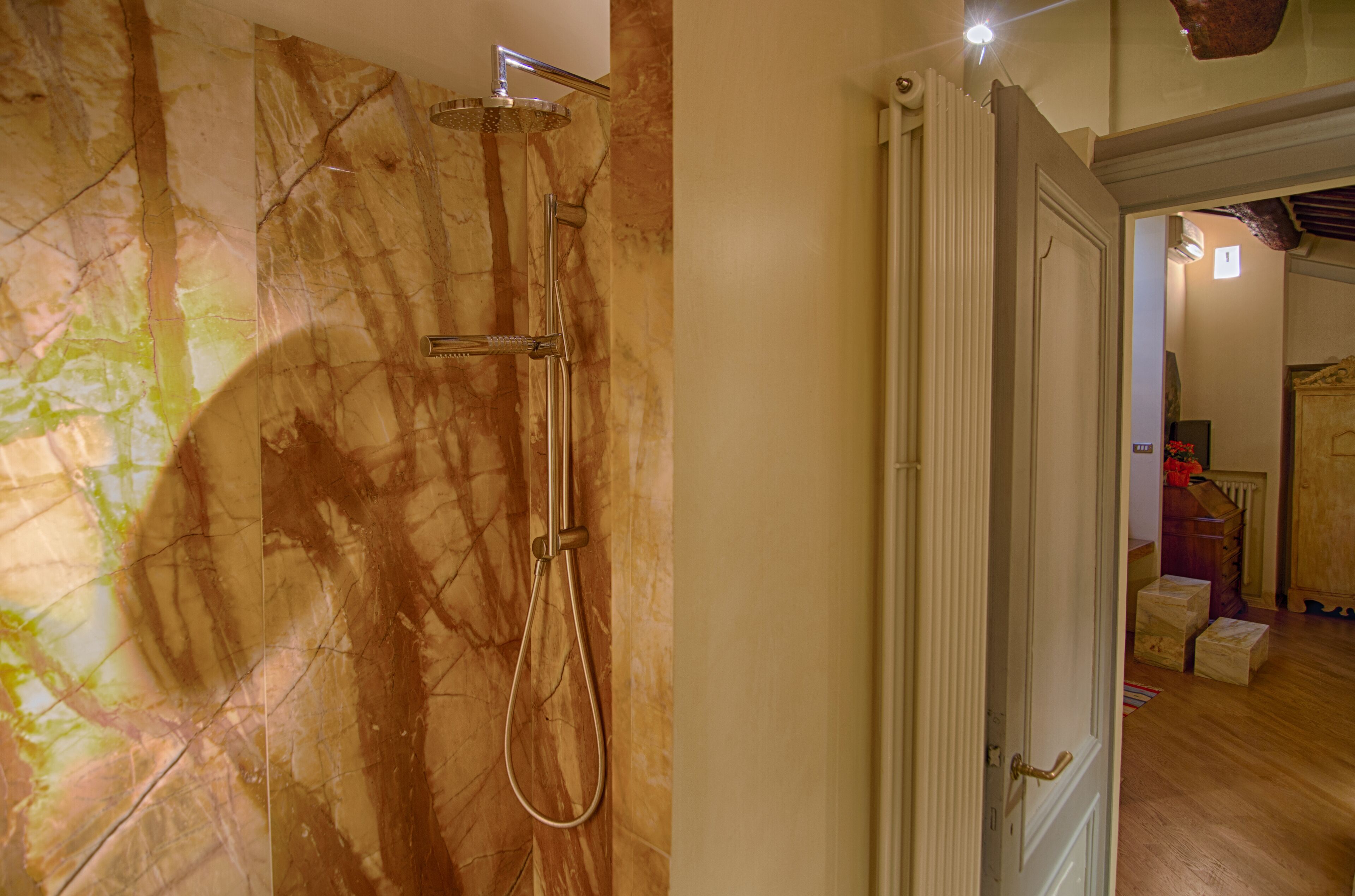 Een badkamer met een marmeren wand, een douche en een houten vloer.