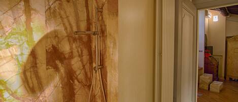 Een badkamer met een marmeren wand, een douche en een houten vloer.