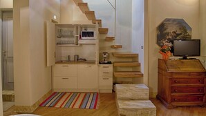 A compact kitchen with a microwave, coffee maker, and wooden shelves. - Rinidia Siena Centro (Siena)