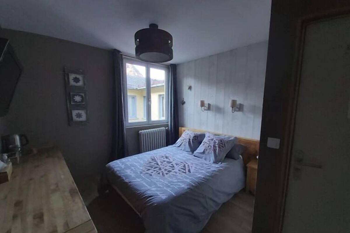 A bedroom with a bed, a window, a radiator, and a wooden dresser.