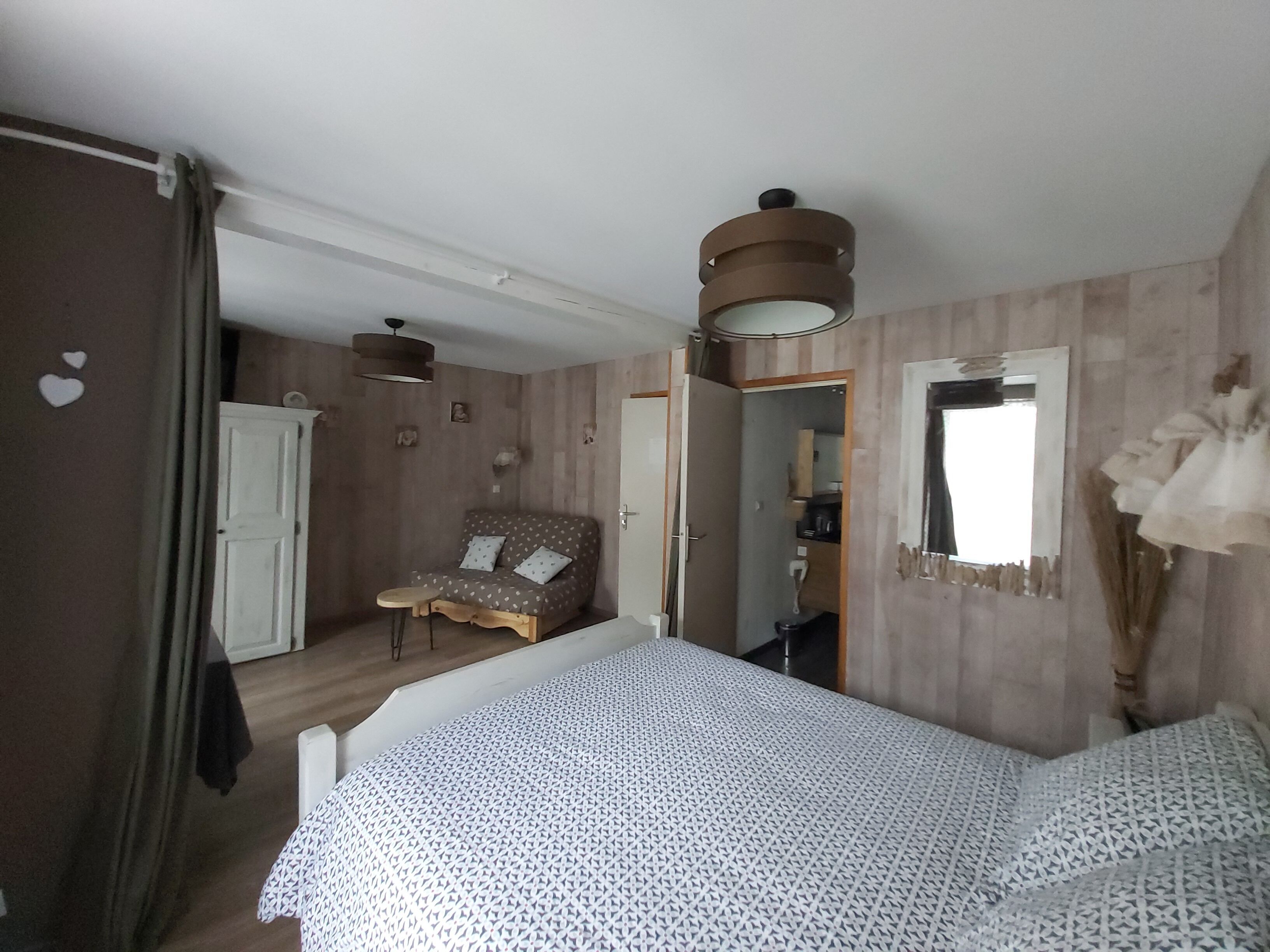 Een slaapkamer met een bed, een stoel, een garderobe, een spiegel en een plafondlamp.