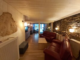 A modern interior with a stone wall, leather sofas, and a wooden ceiling.
