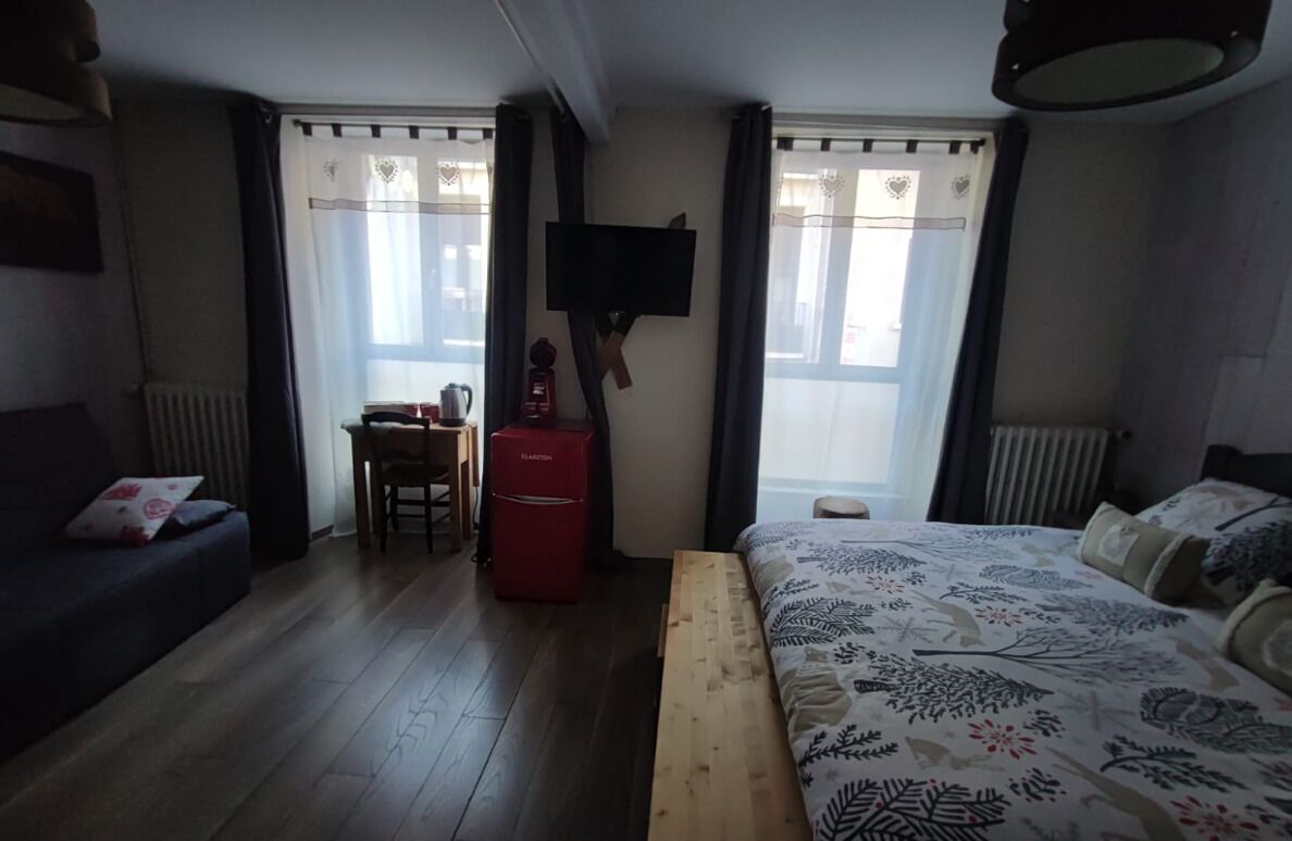 Un dormitorio con cama, un escritorio con silla, un calefactor rojo y un televisor fijado a la pared.