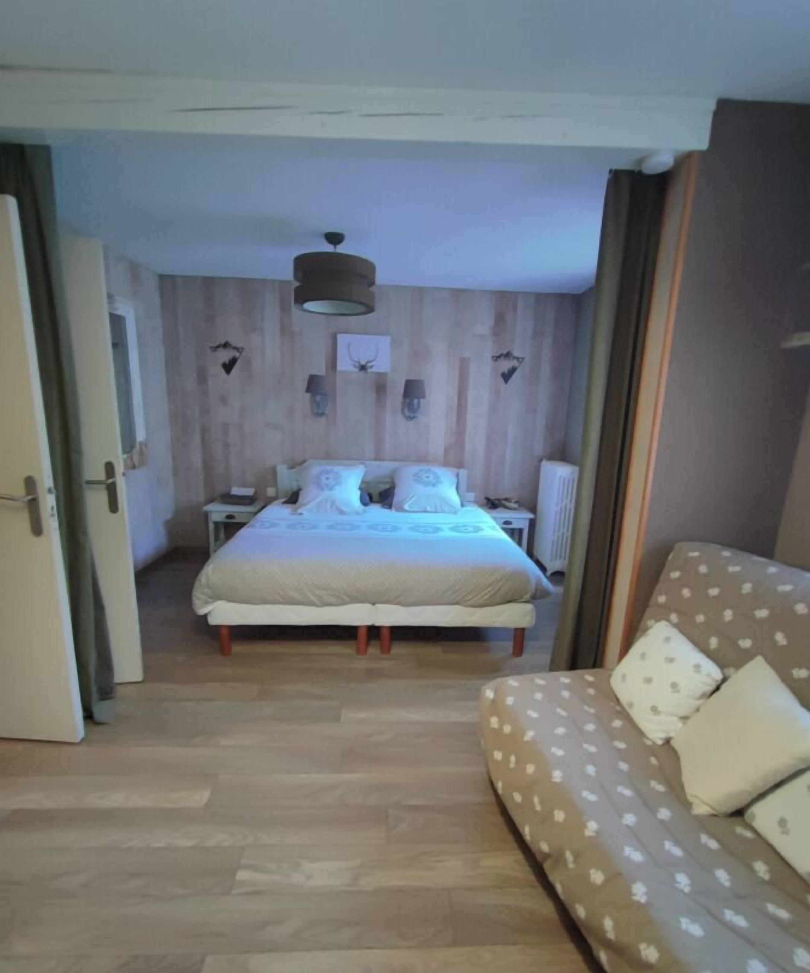 A bedroom with a wooden wall, a bed with white bedding, a nightstand, a lamp, and a window.