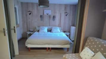 A bedroom with a wooden wall, a bed with white bedding, a nightstand, a lamp, and a window.