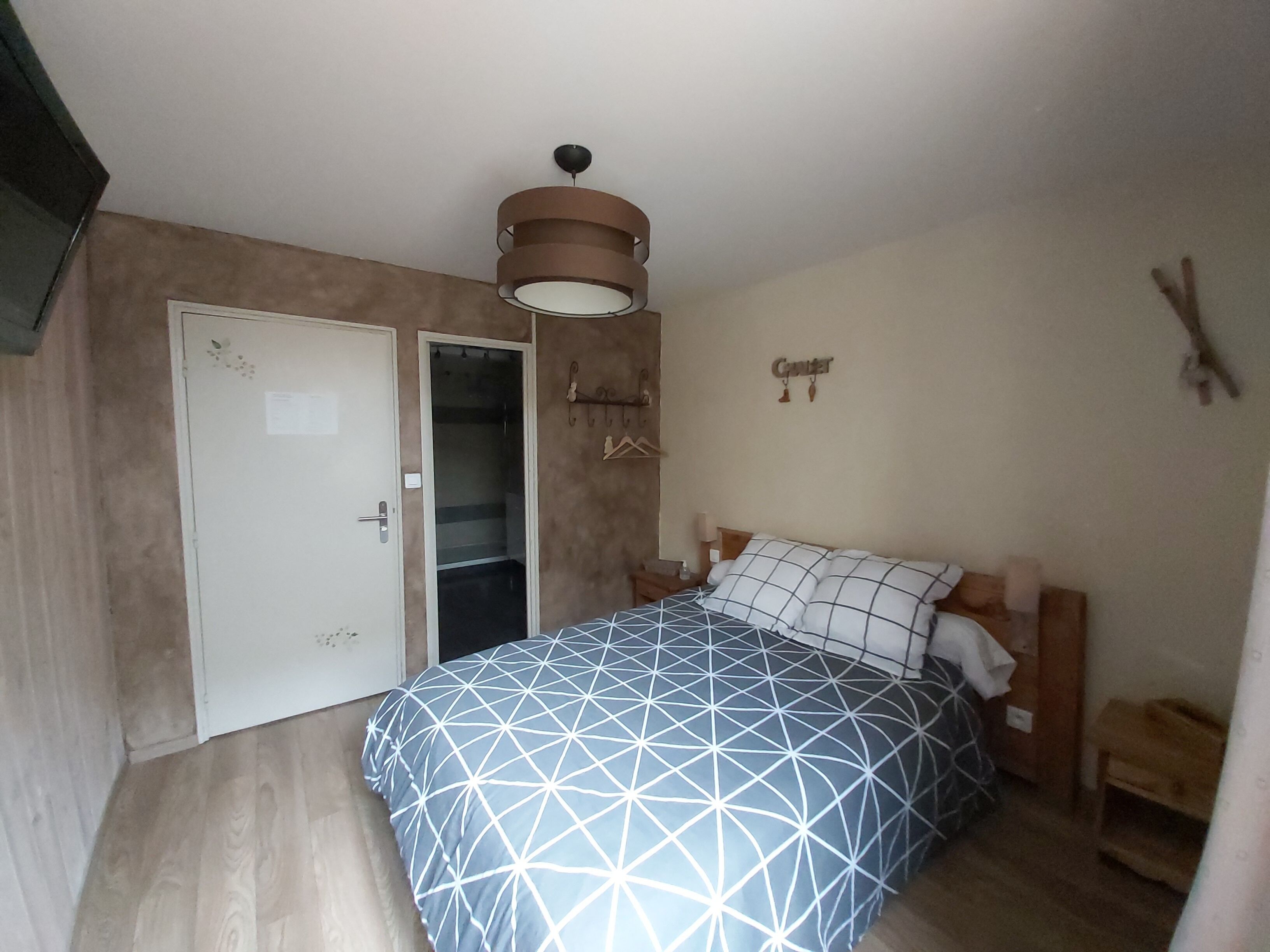 Un dormitorio con cama, armario, perchero y lámpara en el techo.