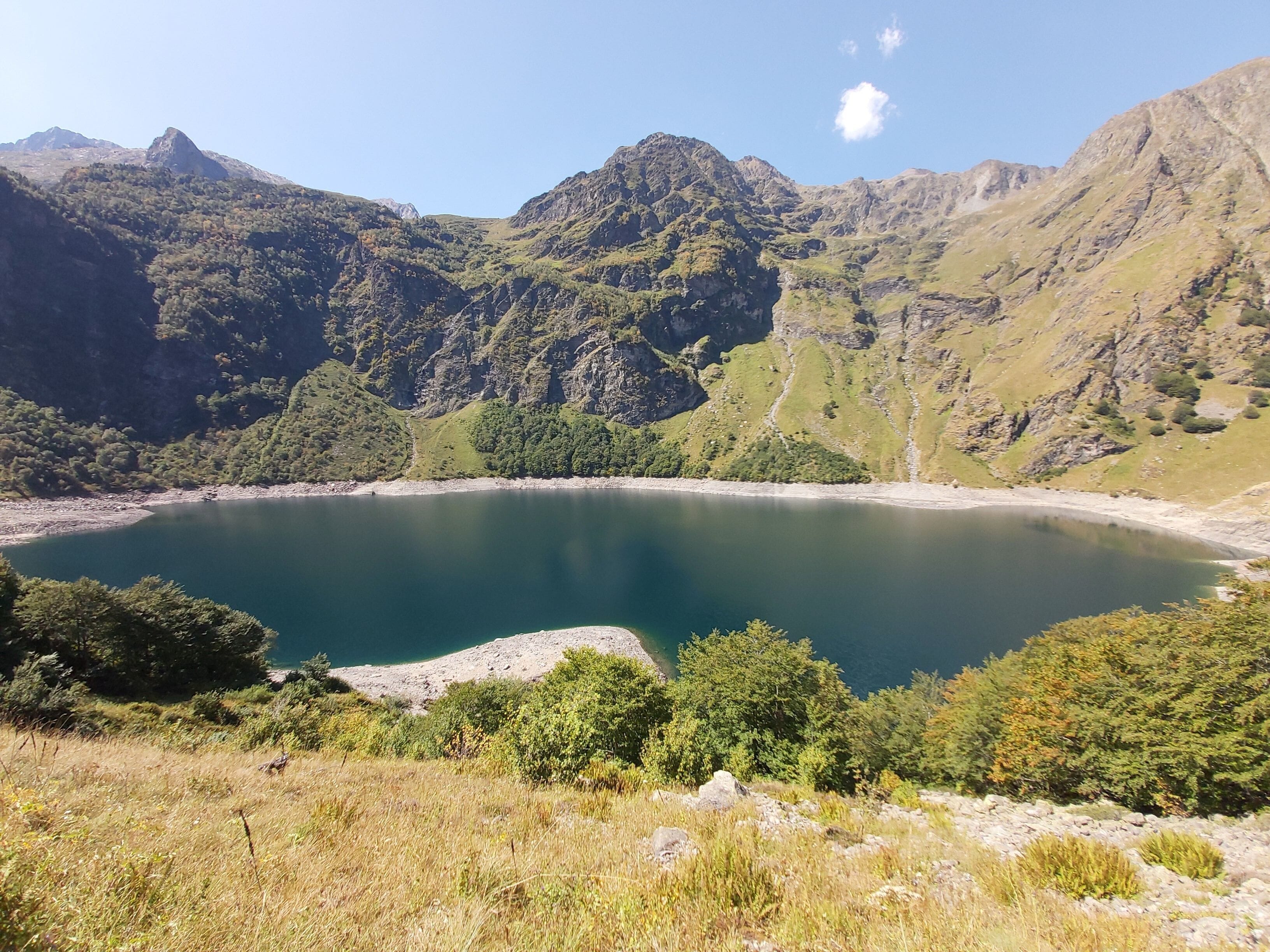 En sjö omgiven av berg med tät vegetation och ett bergigt landskap.