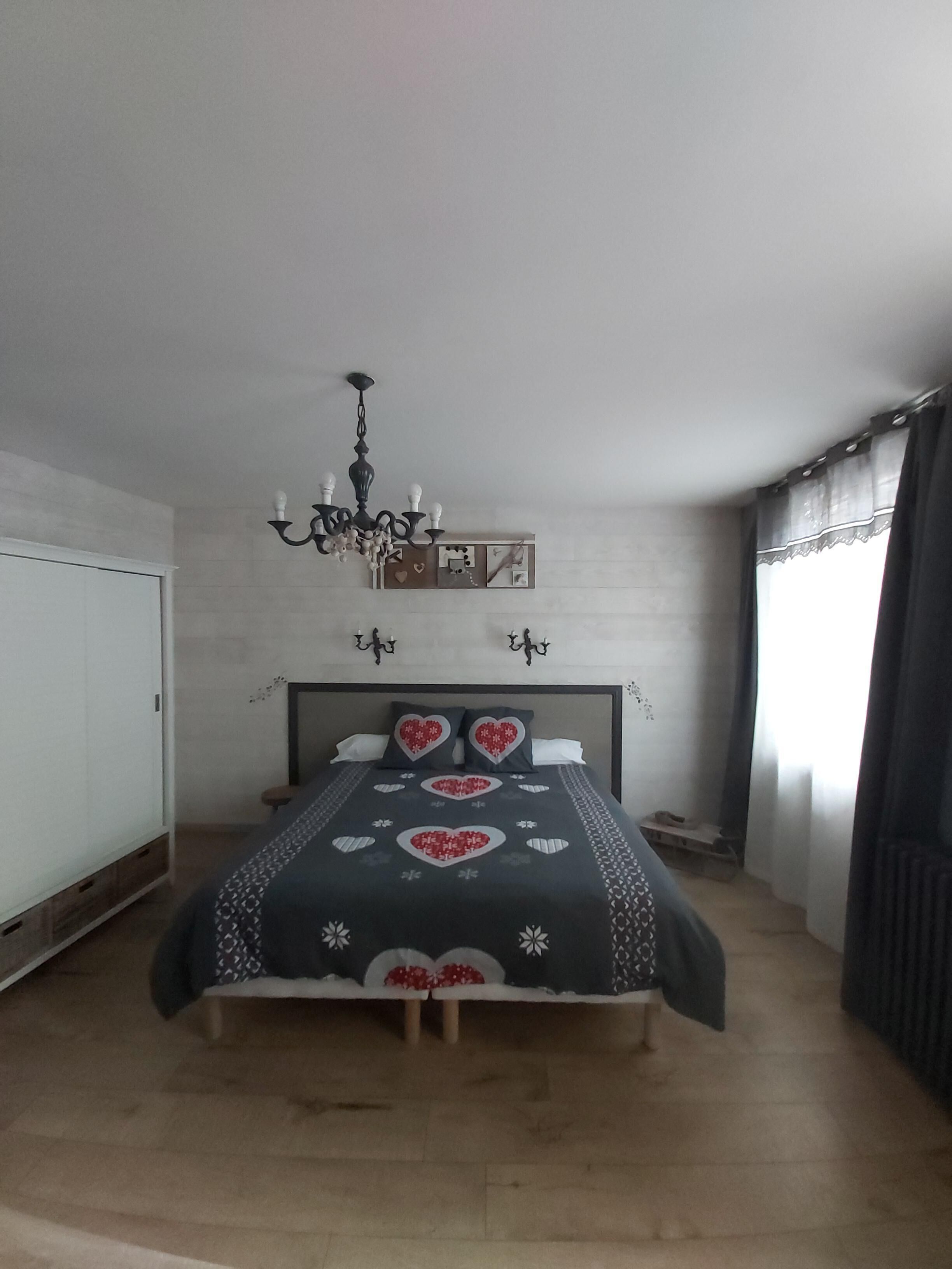 A bedroom with a bed, a chandelier, a wardrobe, and a window with curtains.