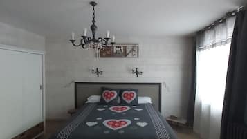 A bedroom with a bed, a chandelier, a wardrobe, and a window with curtains.