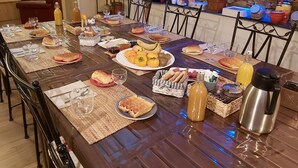 A dining table set with various foods and drinks, surrounded by chairs and a stone wall in the background. - Le Patio de Luchon (Bagneres-de-Luchon)