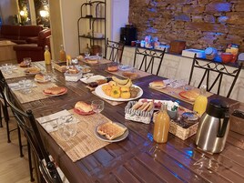 A dining table set with various foods and drinks, surrounded by chairs and a stone wall in the background.