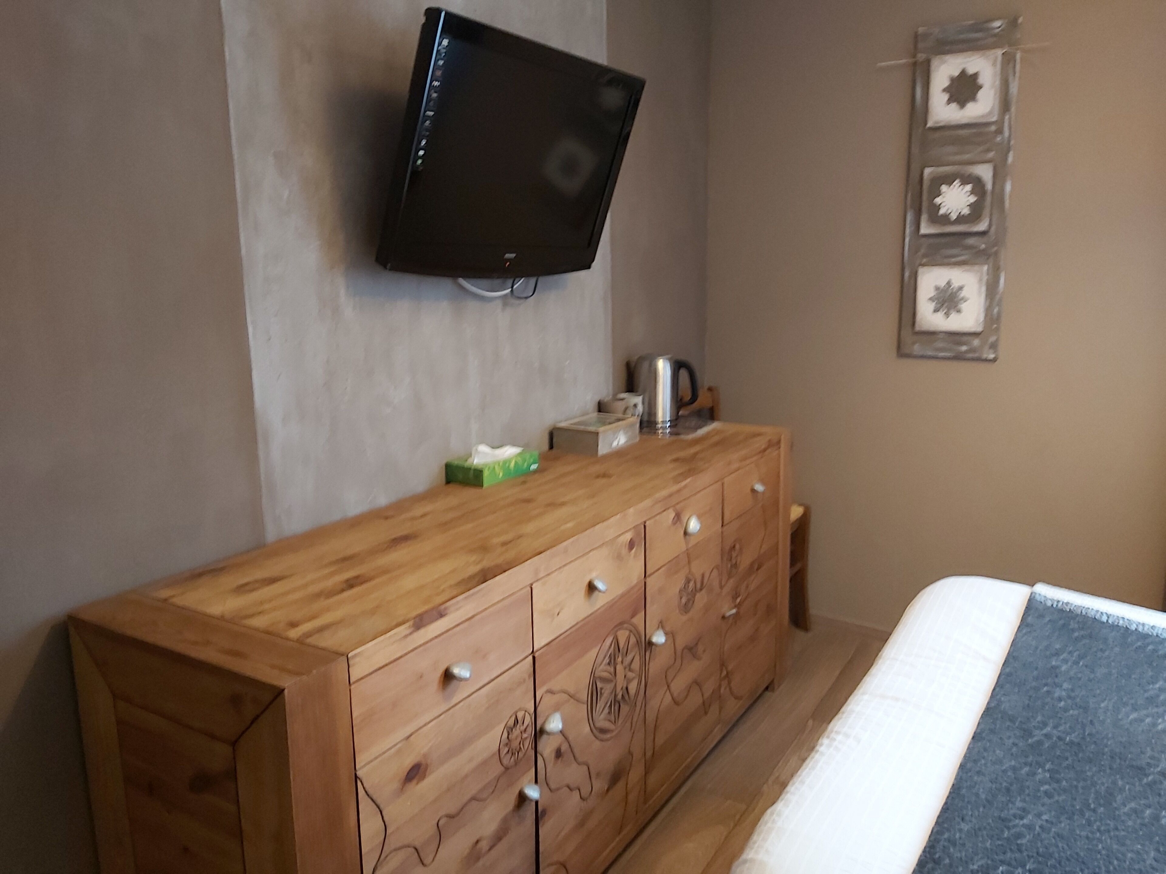 Un dormitorio con un aparador de madera, un televisor montado en la pared y una cama con una manta azul.