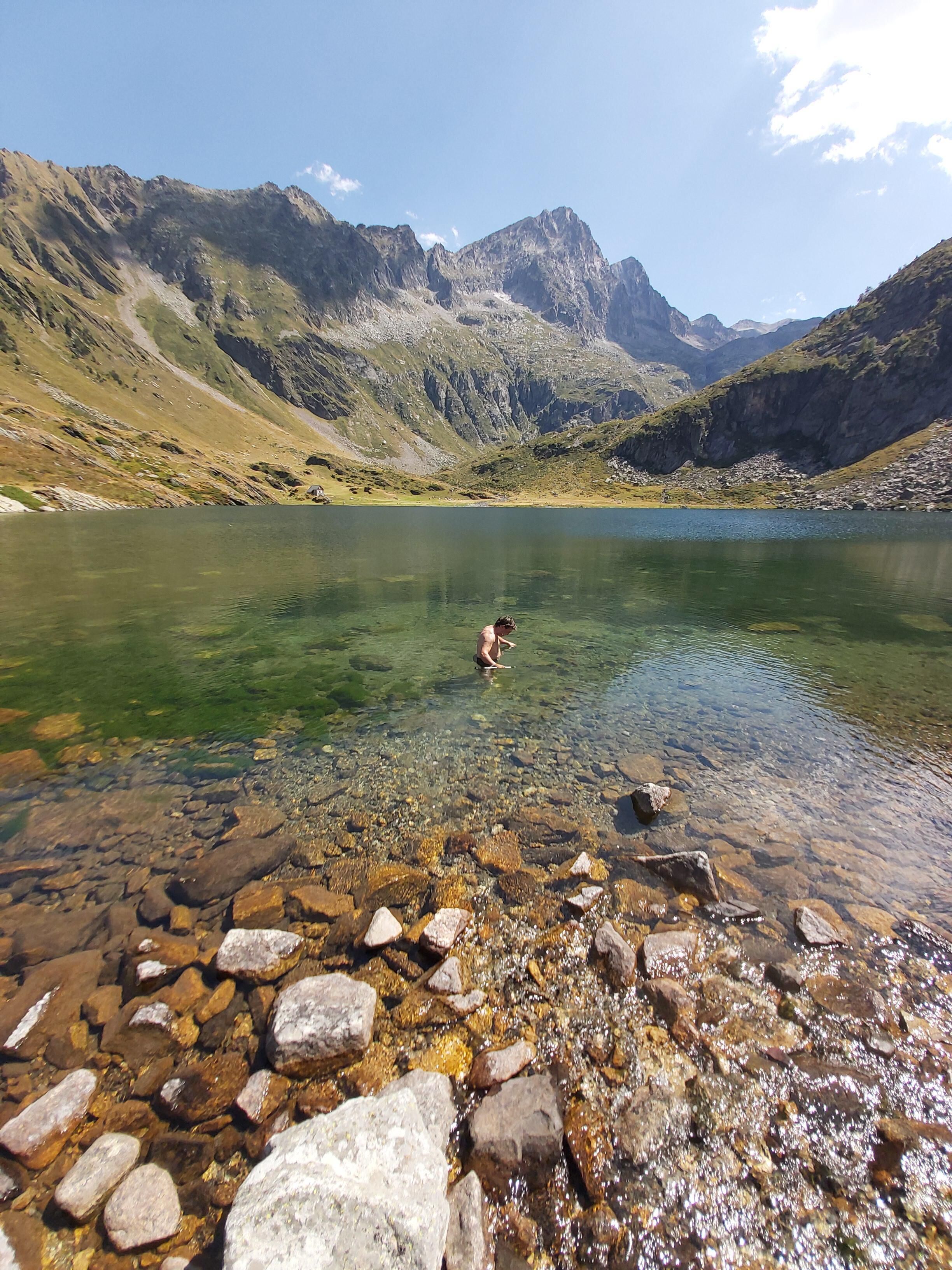 Een helder bergmeer met rotsachtige oevers en iemand in het water.