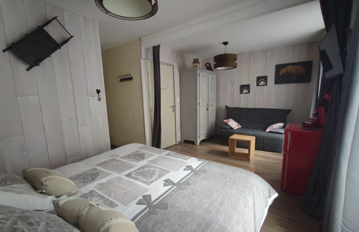 Un dormitorio con una cama, un taburete de madera, un armario y un electrodoméstico rojo.
