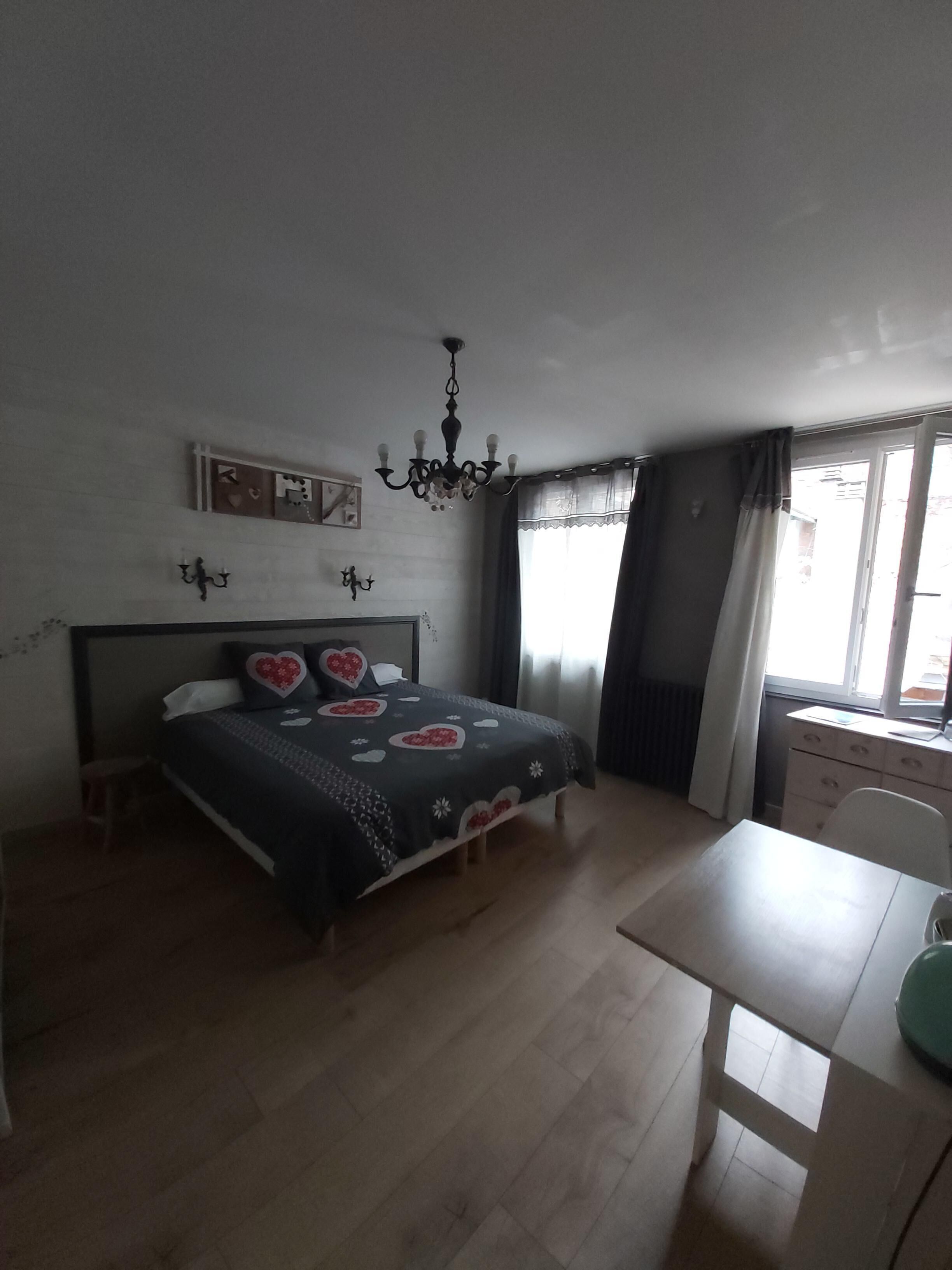 A bedroom with a bed, a desk, a chair, a chandelier, and a window with curtains.