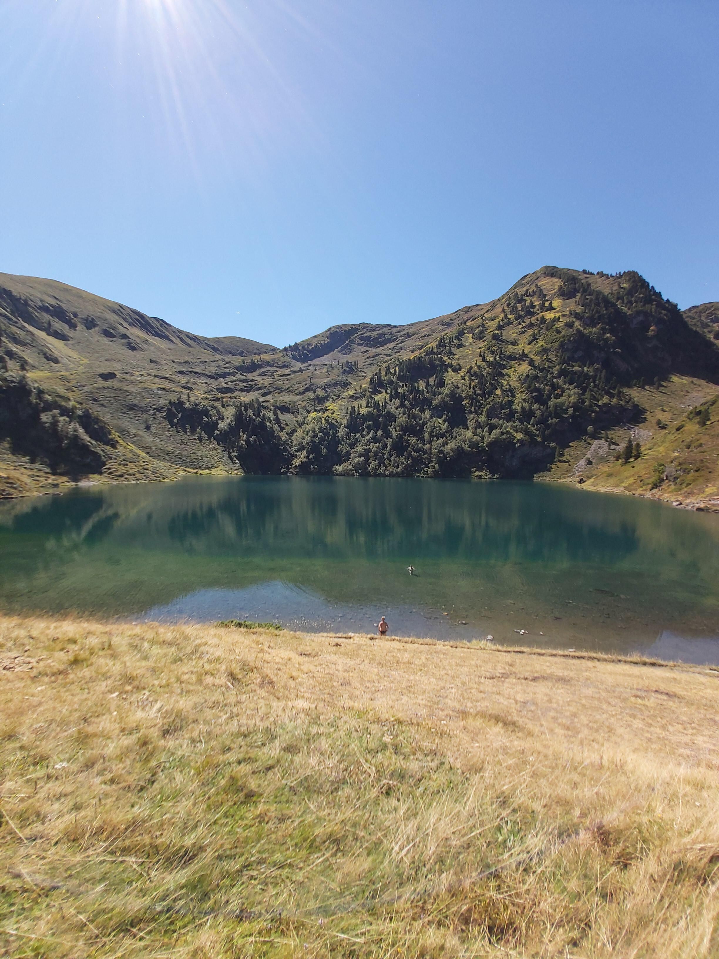 A clear view of a lake surrounded by hills with a person standing by the water's edge.