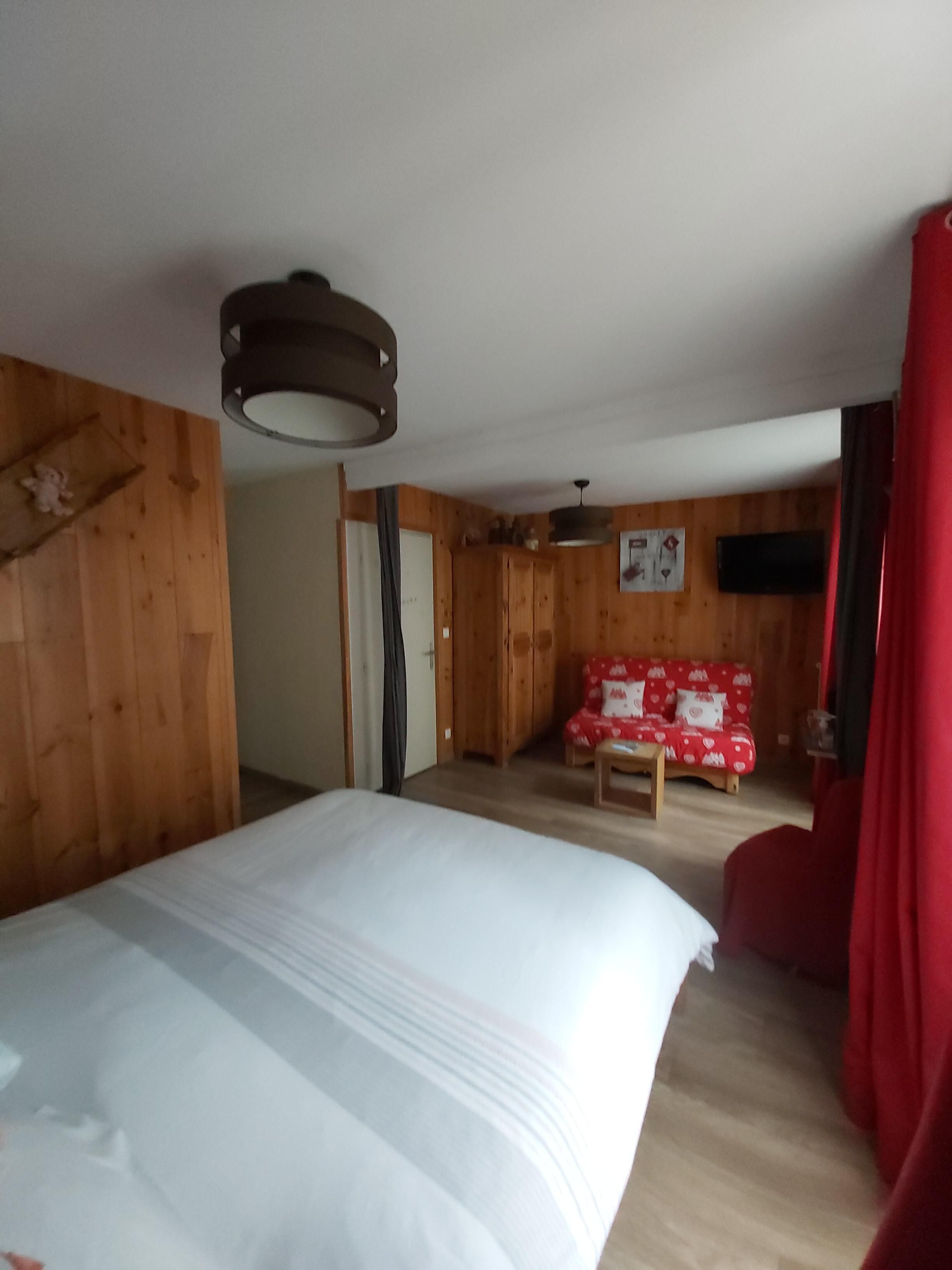 A room with a bed, a red chair, a wooden wall, and a television.