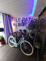 A room with a bicycle, plants, and a sign reading "LE PATIO".