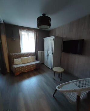 Et lille, hyggeligt værelse med en sofa, et lille bord, en radiator og et TV ophængt på væggen.