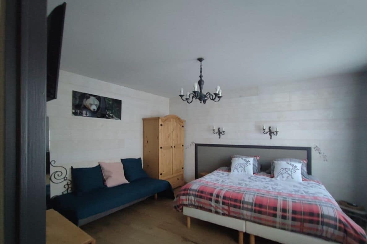 Een slaapkamer met een bed, een houten garderobe, een blauwe bank, een kroonluchter en wandlampen.