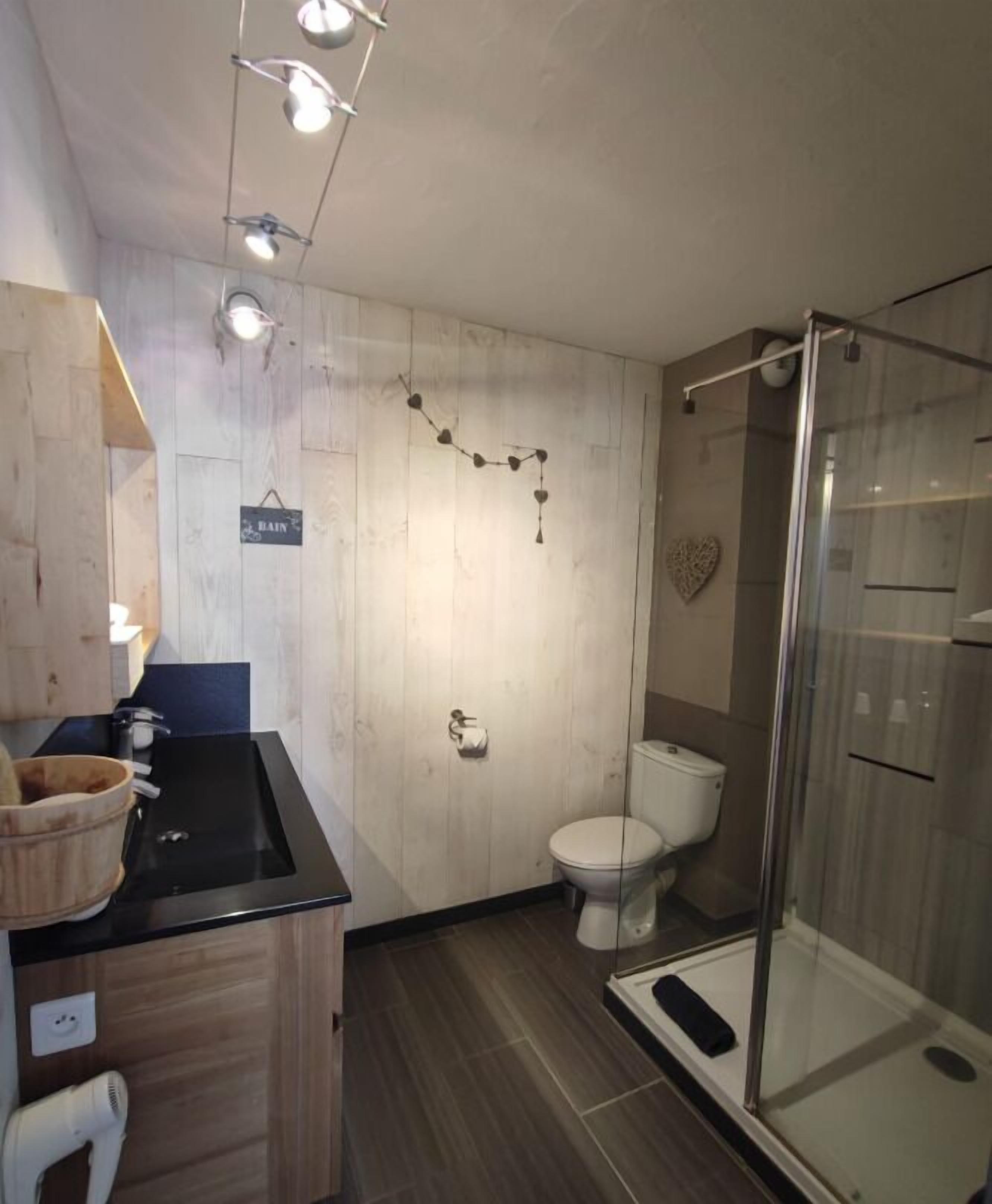 A bathroom with a wooden vanity, a toilet, a glass shower enclosure, and a wall-mounted towel rack.