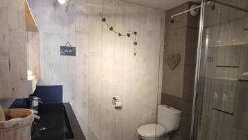A bathroom with a wooden vanity, a toilet, a glass shower enclosure, and a wall-mounted towel rack.