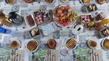 A table set with waffles, fruits, and condiments, with a scenic tablecloth.