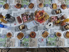 A table set with waffles, fruits, and condiments, with a scenic tablecloth. - Le Patio de Luchon (Bagneres-de-Luchon)