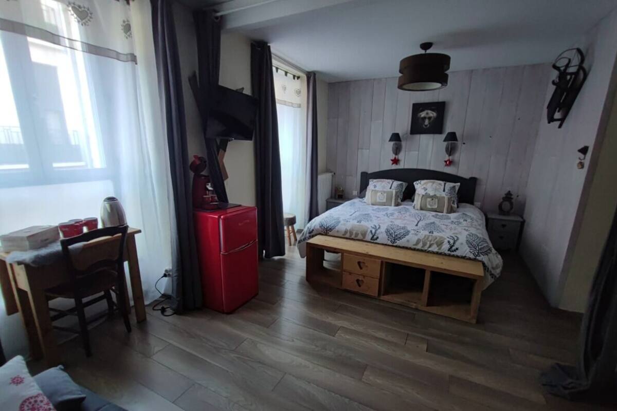 A bedroom with a wooden bed, a desk with a red appliance, and a window with curtains.