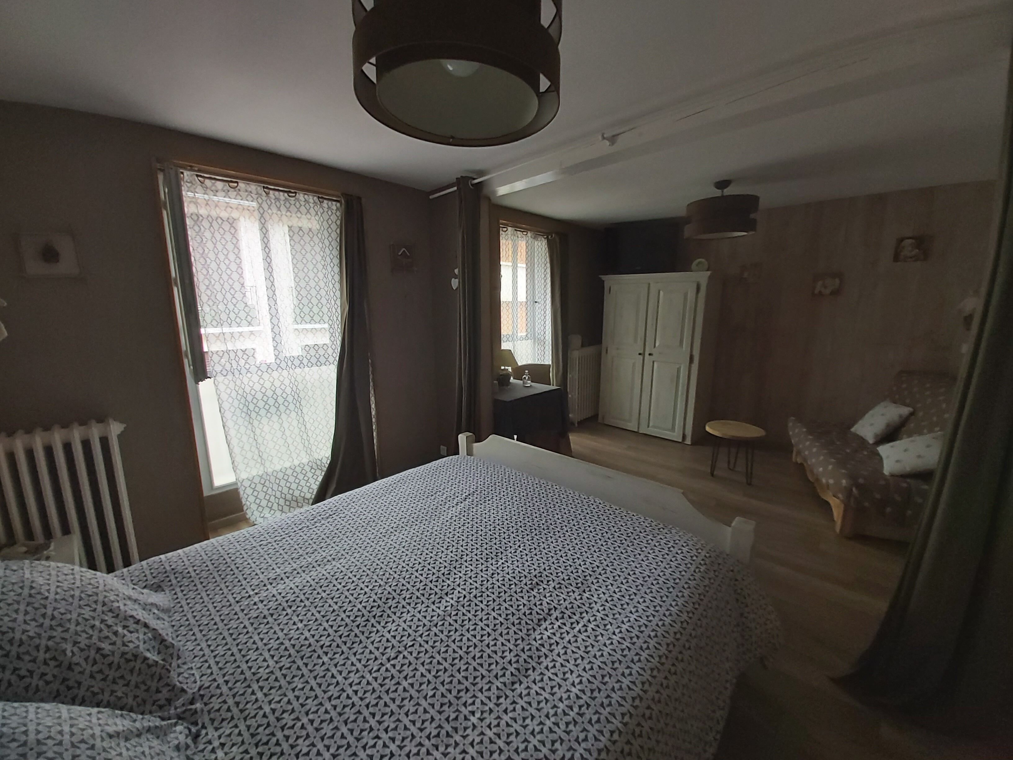 Une chambre à coucher comprenant un lit, une armoire et un petit coin salon avec un fauteuil et des coussins.