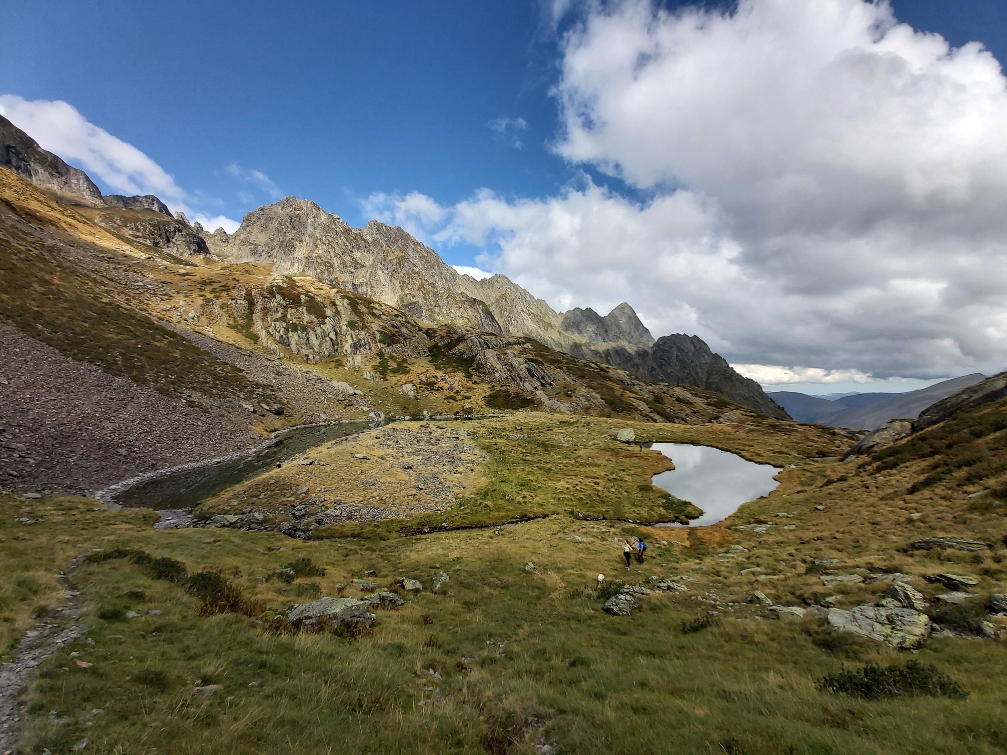Eine gebirgige Landschaft mit blauem Himmel, felsigem Gelände und einem kleinen See.